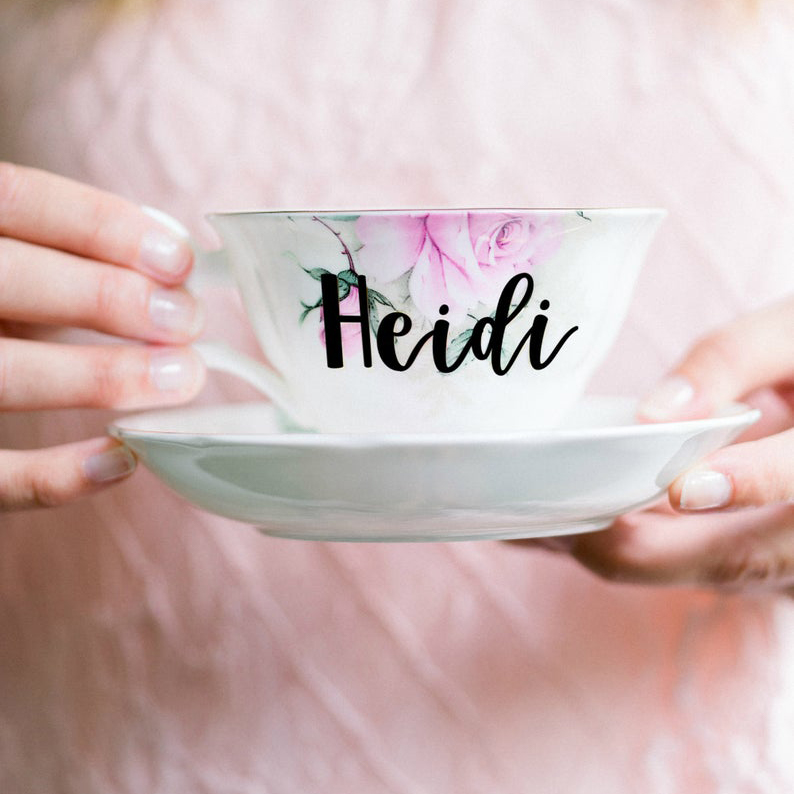 Womans hands holding floral teacup with Heidi in brush lettering