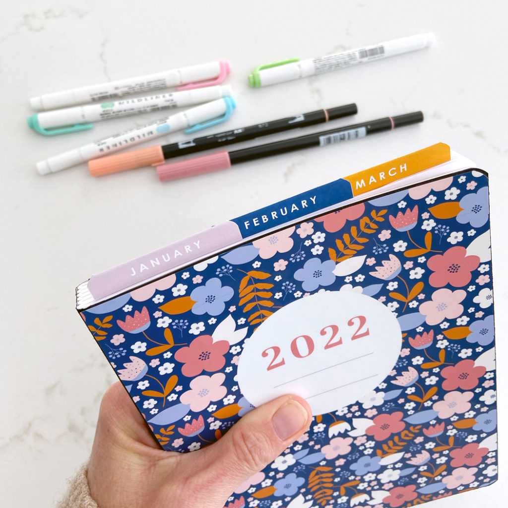 Hand holding notebook with printable cover and page tabs for a focused purposeful bullet journal