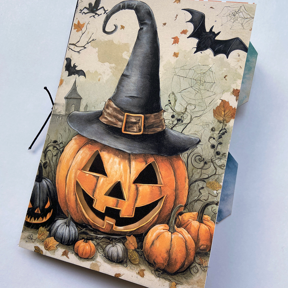 Handmade junk journal showing the cover which features a Jack-O-Lantern pumpkin wearing a black witches hat.