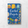 Front cover of Crochet Projects Journal featuring a blue background with various crochet and craft tools around the wording Crochet Projects.